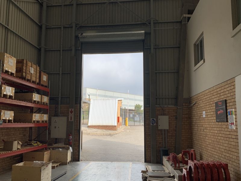 Industrial warehouse space featuring high ceilings, exposed steel structural elements, durable concrete flooring, and a large roller shutter door for vehicle access.