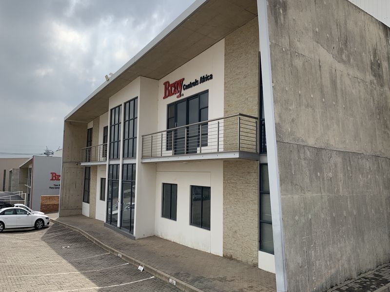 Modern industrial office building featuring exposed concrete, stone cladding, and metal balcony railings with a paved parking area.