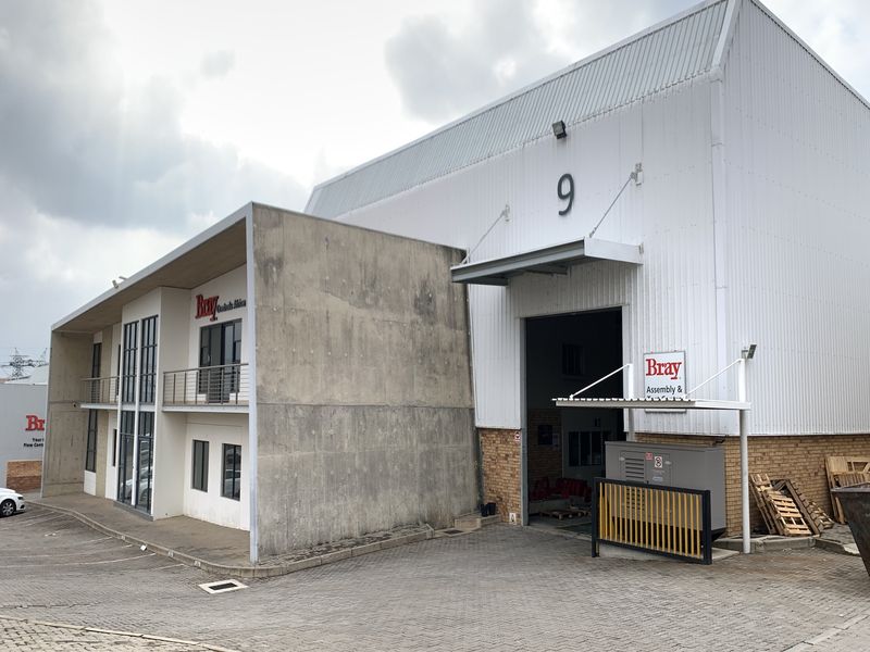 Industrial property featuring a warehouse unit with a large roller door, concrete facade, and attached office space with a balcony.