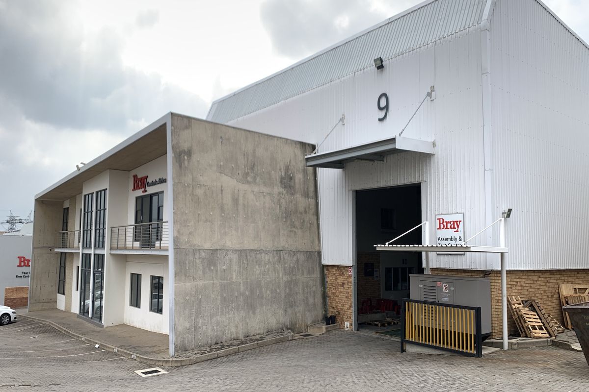 Industrial property featuring a warehouse unit with a large roller door, concrete facade, and attached office space with a balcony.