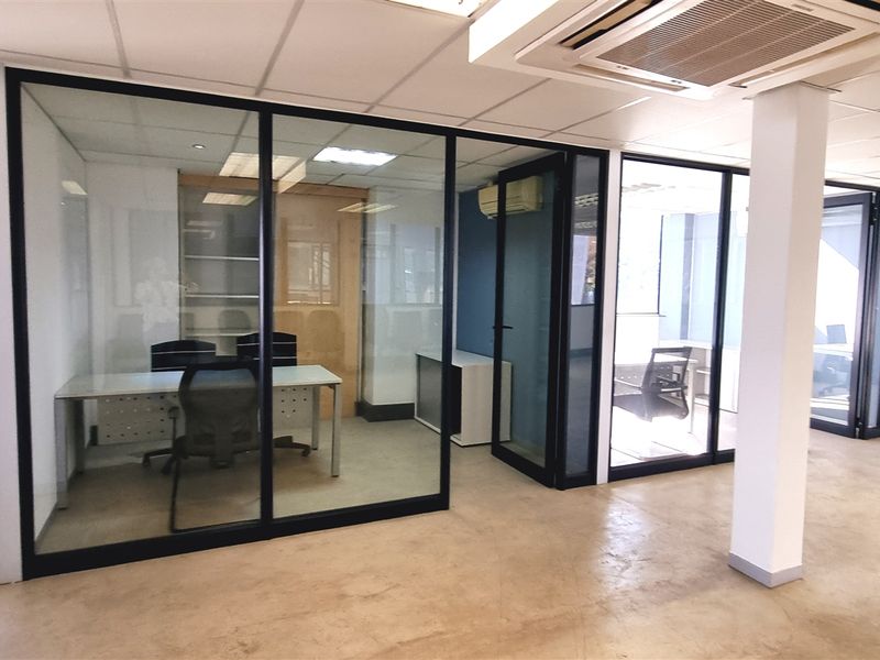 Modern office space featuring glass-partitioned private offices, suspended ceilings with recessed lighting, and polished concrete flooring throughout the open-plan area.