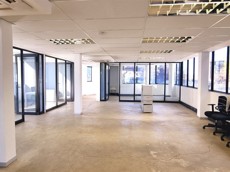 Spacious open-plan office area featuring glass partitioning, large windows for natural light, suspended ceilings, and polished concrete flooring.
