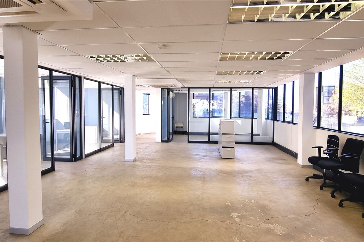 Spacious open-plan office area featuring glass partitioning, large windows for natural light, suspended ceilings, and polished concrete flooring.