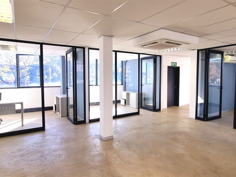 Open-plan office space featuring modern glass partitions, suspended ceilings with recessed lighting, central air conditioning, and polished concrete flooring.
