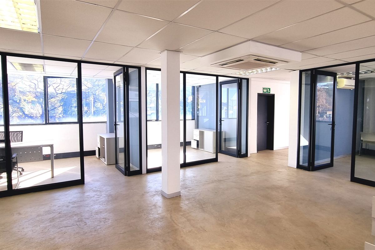 Open-plan office space featuring modern glass partitions, suspended ceilings with recessed lighting, central air conditioning, and polished concrete flooring.
