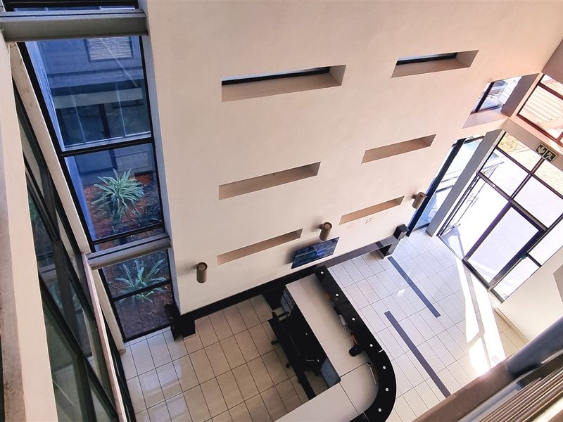 A high-ceilinged office entrance lobby featuring a modern reception desk, expansive glass windows, and tiled flooring with a bright, open-plan layout.
