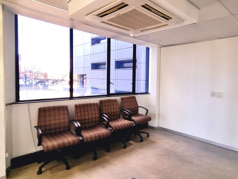 A functional office space featuring a large window, suspended ceiling with integrated air conditioning, and recessed lighting, suitable for a professional work environment.