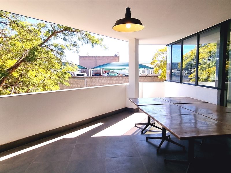 A spacious covered balcony featuring tiled flooring, modern pendant lighting, and large glass windows overlooking the surrounding area.