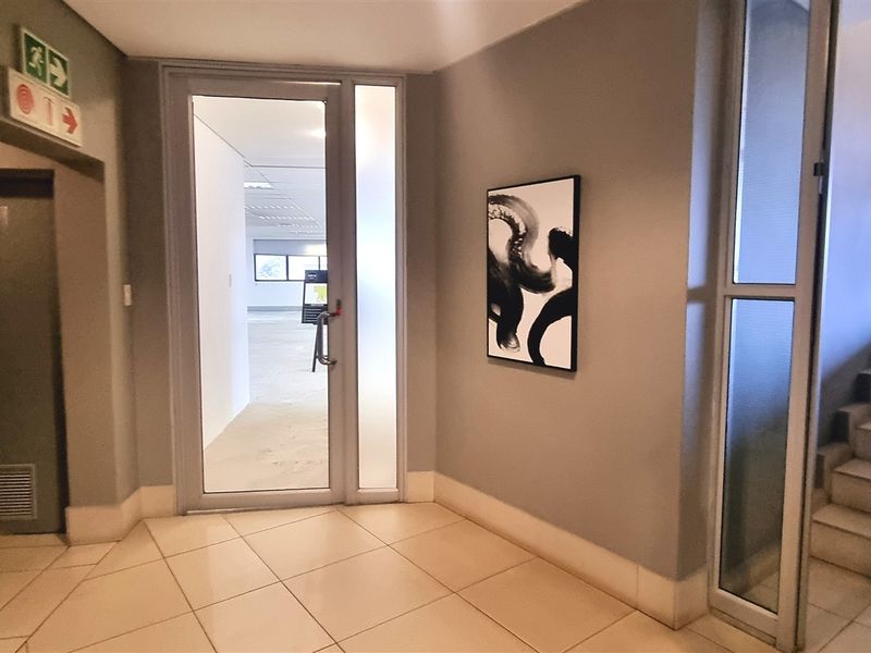 A clean office building entrance lobby featuring tiled flooring, a glass entry door, and a staircase leading to upper levels.
