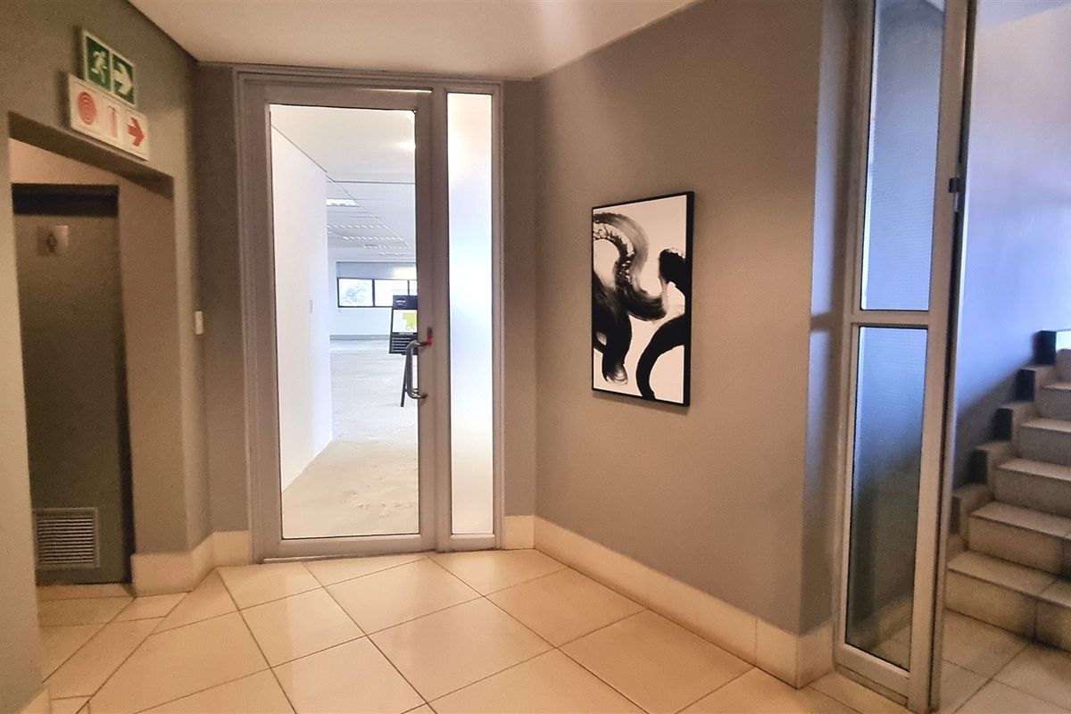 A clean office building entrance lobby featuring tiled flooring, a glass entry door, and a staircase leading to upper levels.