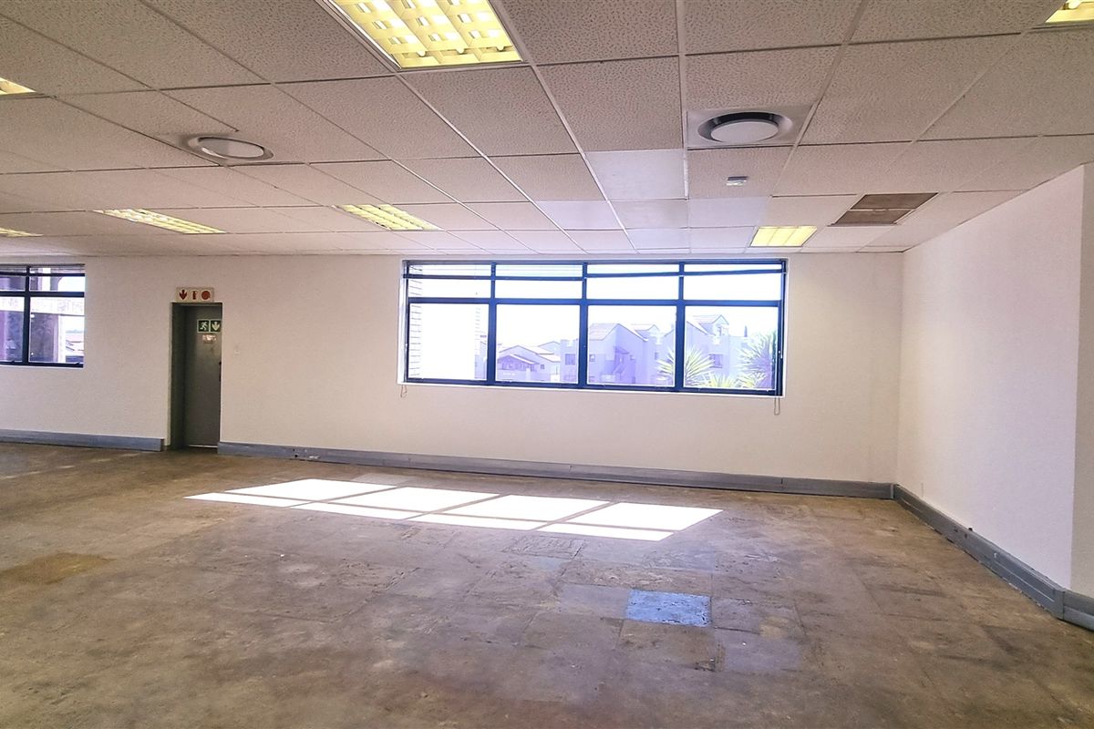 Spacious open-plan office area featuring a suspended ceiling, recessed lighting, and large windows providing ample natural light, with concrete flooring throughout.