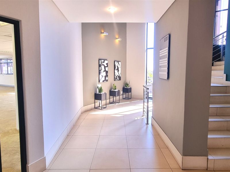 A bright and modern office building entrance lobby featuring tiled flooring, a staircase with a metal handrail, and large windows providing natural light.
