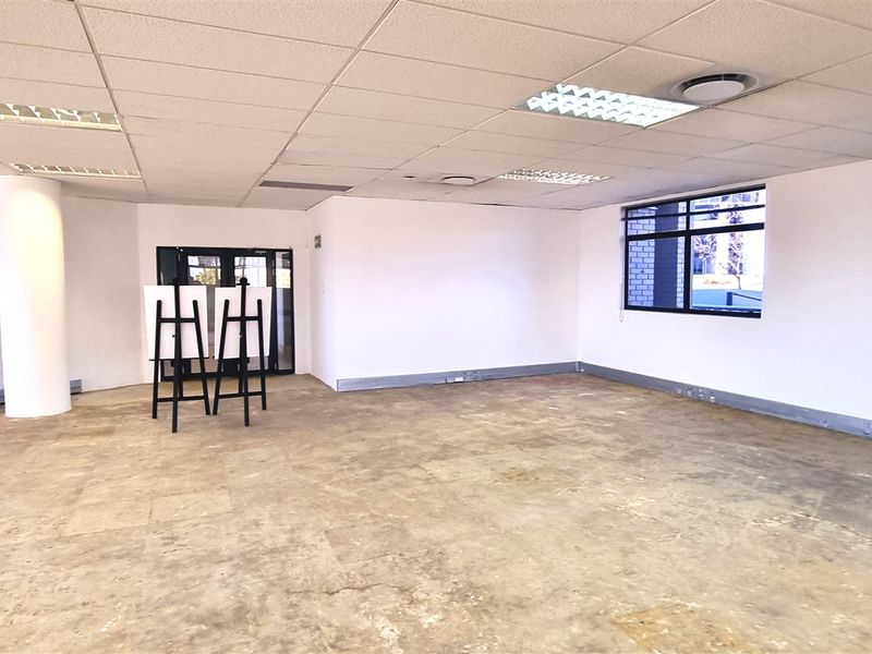 An open-plan office space featuring a suspended ceiling, recessed lighting, central air conditioning, and large windows, currently presented as a vacant shell.