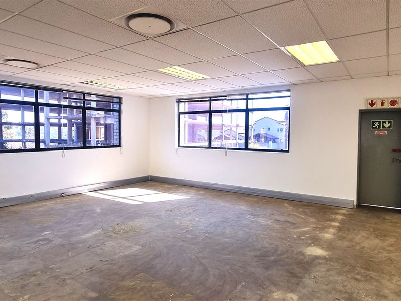 An empty, open-plan office space featuring suspended ceilings, recessed lighting, and large windows, currently requiring flooring and wall finish updates.