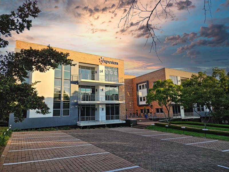 A professional multi-story office building featuring modern architectural design, glass balconies, and a paved parking area set within a landscaped environment.
