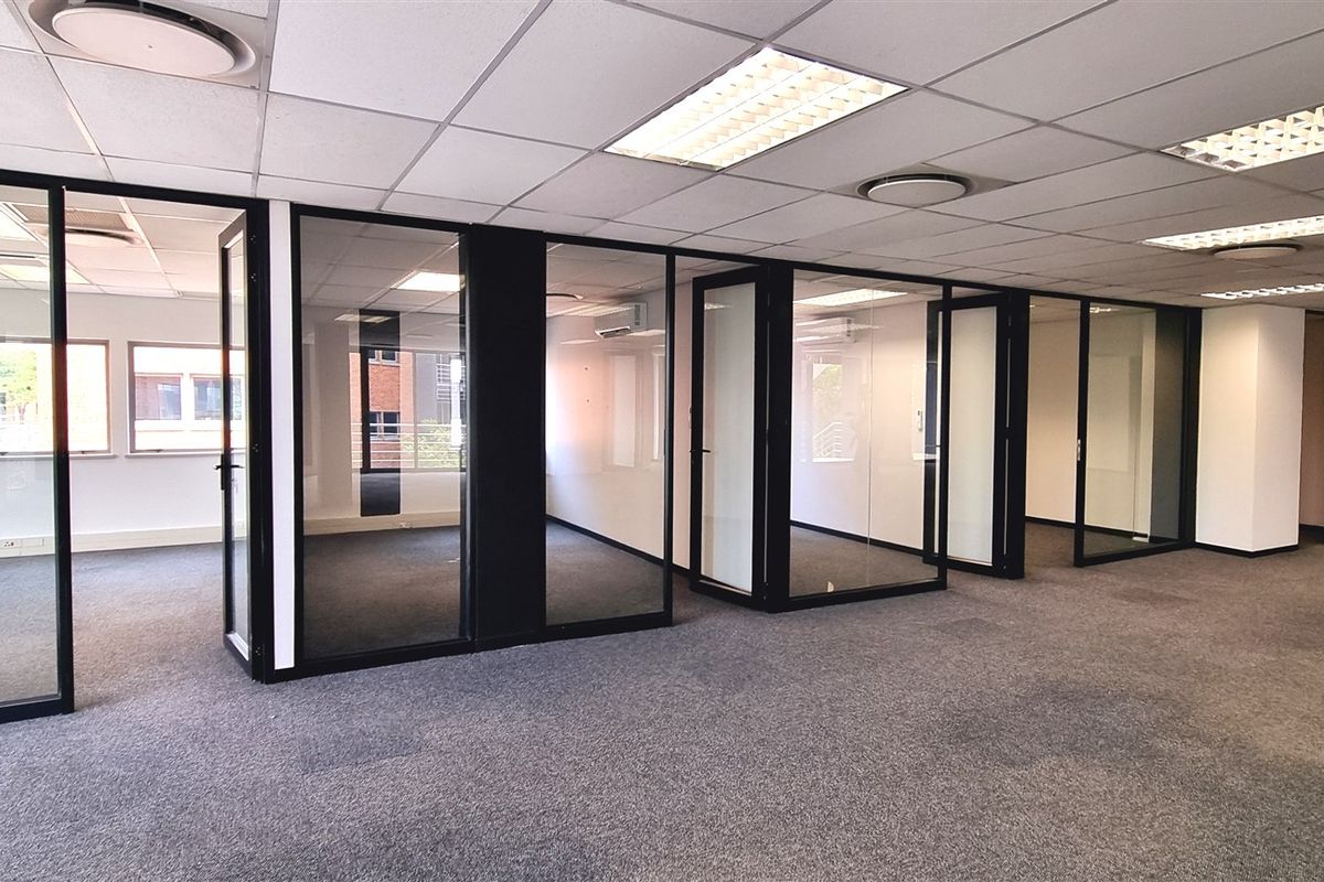 Open plan office space featuring glass partitioned private offices, suspended ceilings with recessed lighting, and carpeted flooring throughout.