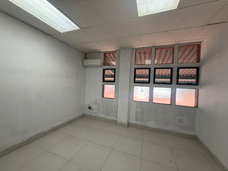 A vacant office space featuring tiled flooring, a drop ceiling with integrated lighting, and a wall-mounted air conditioning unit.