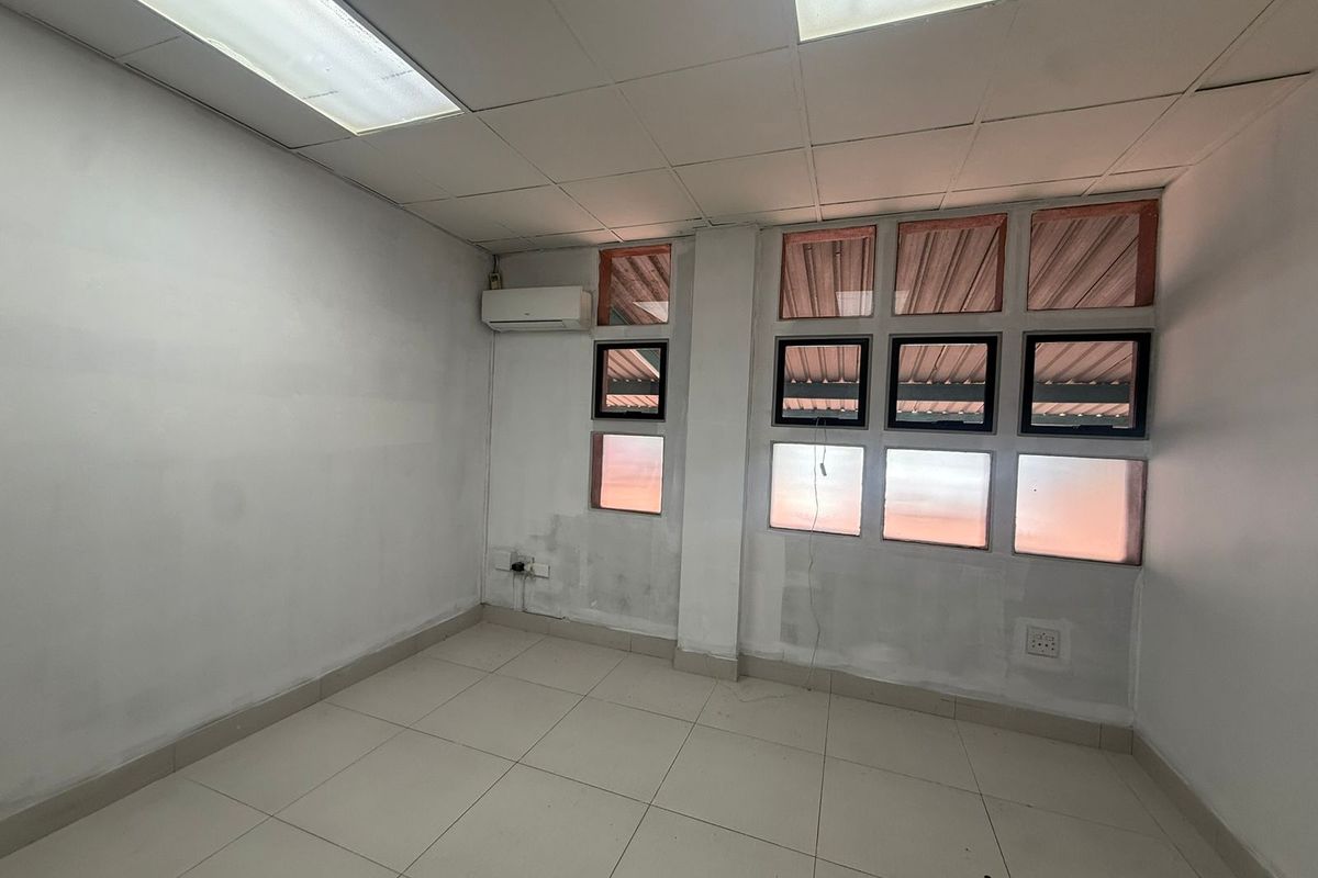 A vacant office space featuring tiled flooring, a drop ceiling with integrated lighting, and a wall-mounted air conditioning unit.