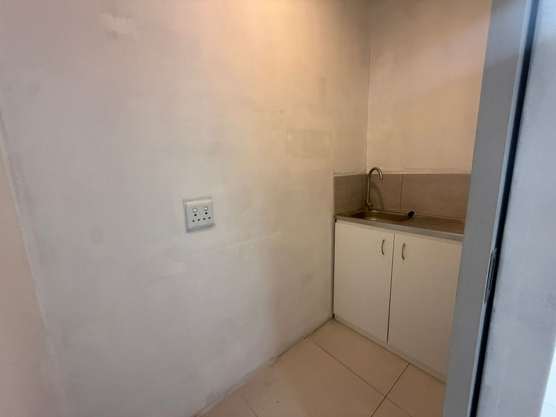 A compact utility space featuring a small built-in kitchenette cabinet with a stainless steel sink and faucet.