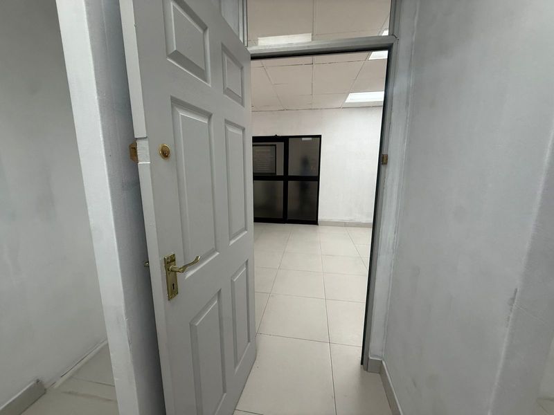 A view through an open doorway into a vacant office space featuring tiled flooring and a suspended ceiling grid.