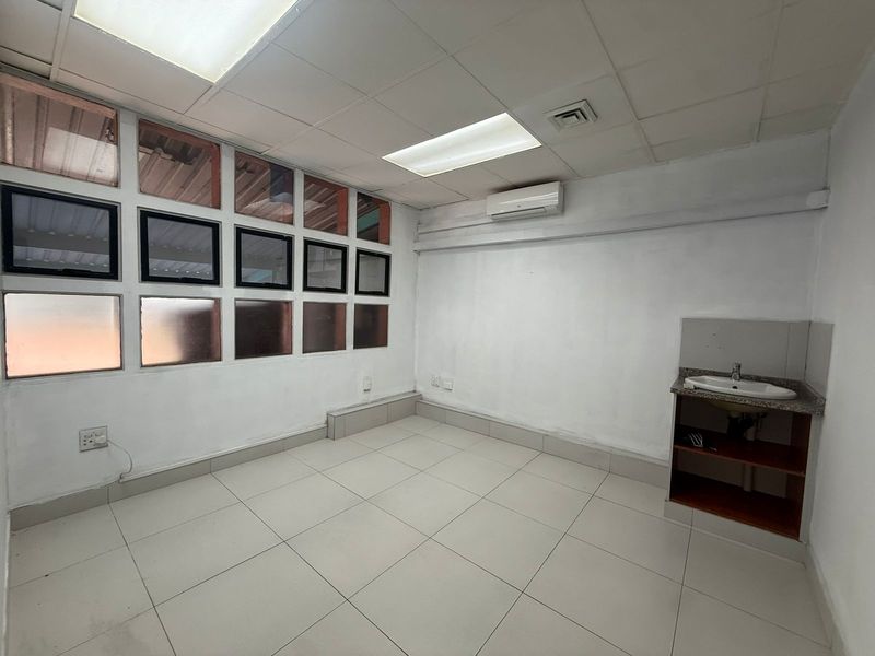 A functional office space featuring tiled flooring, a built-in vanity sink, recessed ceiling lighting, and a wall-mounted air conditioning unit.