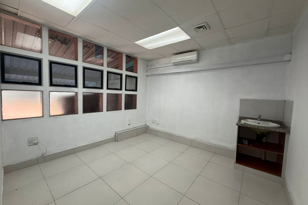 A functional office space featuring tiled flooring, a built-in vanity sink, recessed ceiling lighting, and a wall-mounted air conditioning unit.