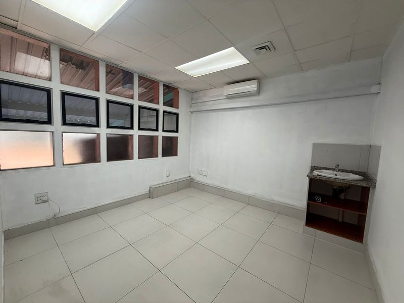 A functional office space featuring tiled flooring, a built-in vanity sink, recessed ceiling lighting, and a wall-mounted air conditioning unit.