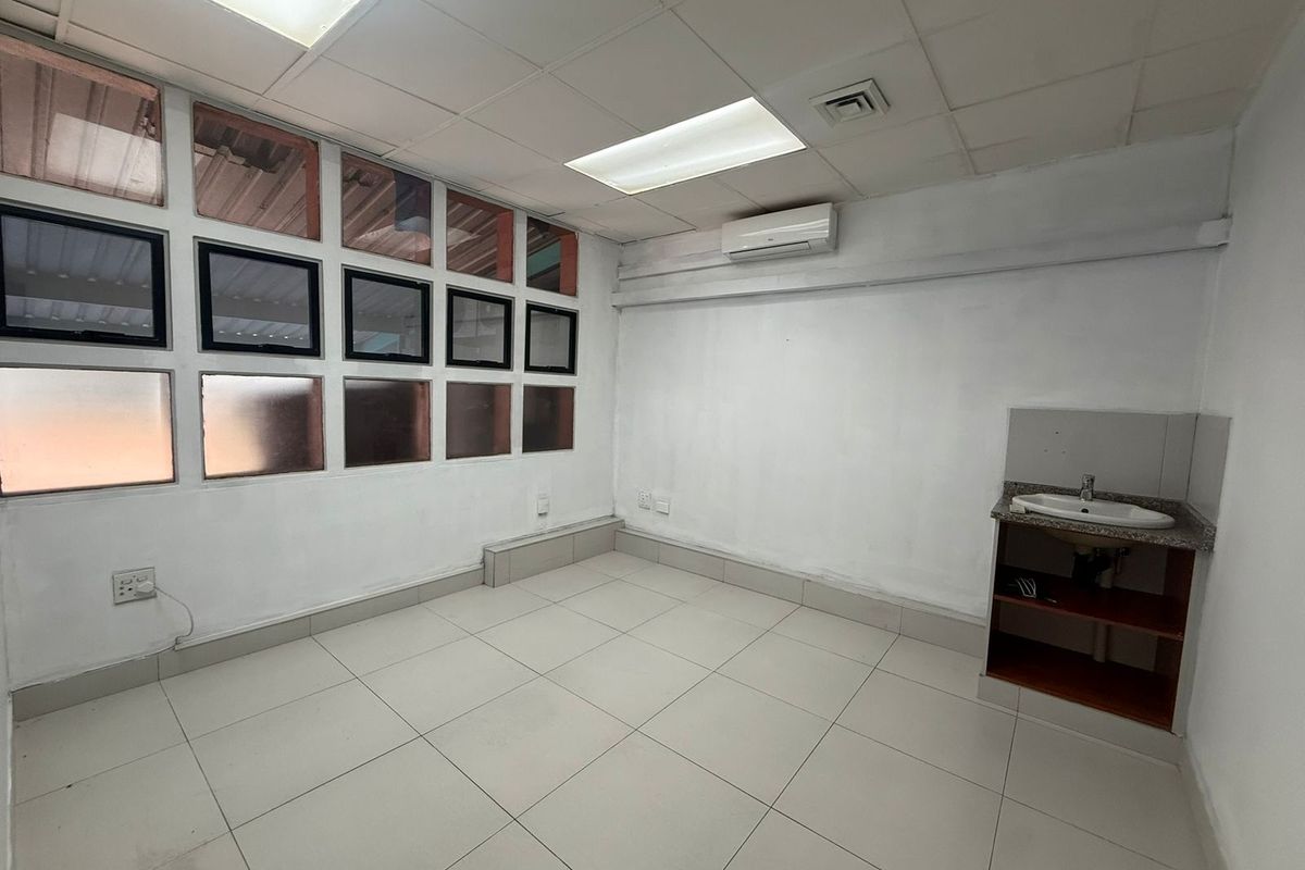 A functional office space featuring tiled flooring, a built-in vanity sink, recessed ceiling lighting, and a wall-mounted air conditioning unit.