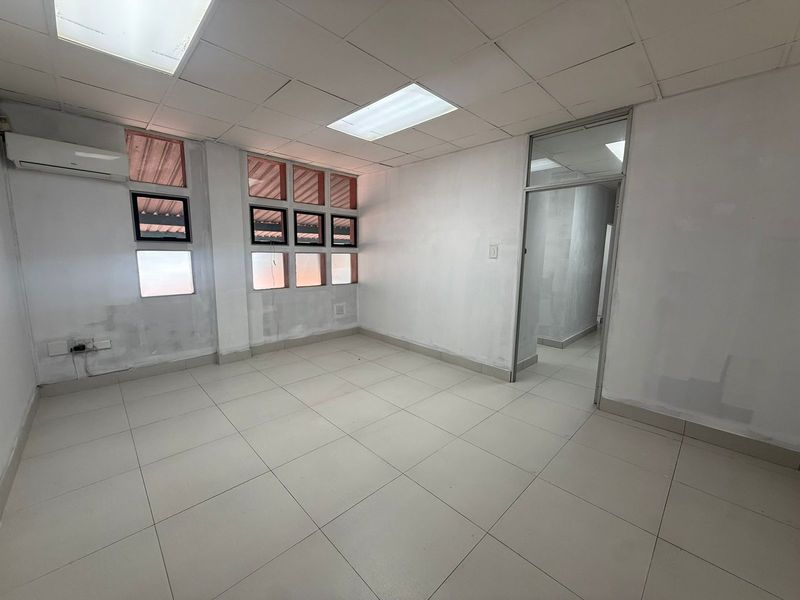 A vacant office space featuring tiled flooring, a drop ceiling with recessed lighting, and a wall-mounted air conditioning unit.