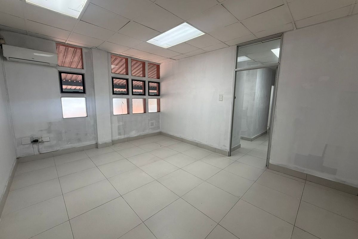 A vacant office space featuring tiled flooring, a drop ceiling with recessed lighting, and a wall-mounted air conditioning unit.