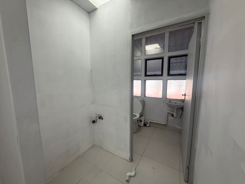 A small, unfinished utility space leading into a basic bathroom with a toilet and wall-mounted basin.