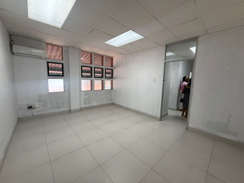 A vacant office space featuring tiled flooring, a drop ceiling with recessed lighting, and a wall-mounted air conditioning unit.