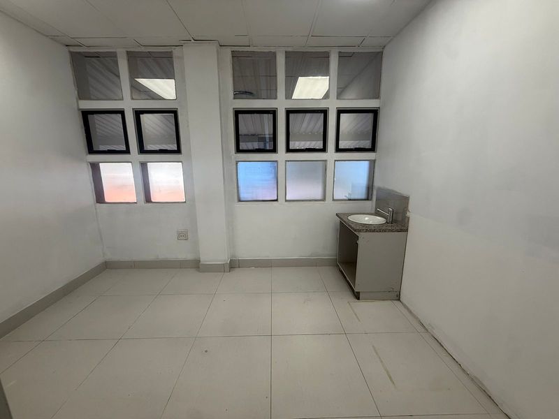 A vacant office space featuring tiled flooring, multiple windows for natural light, and a built-in vanity sink unit.