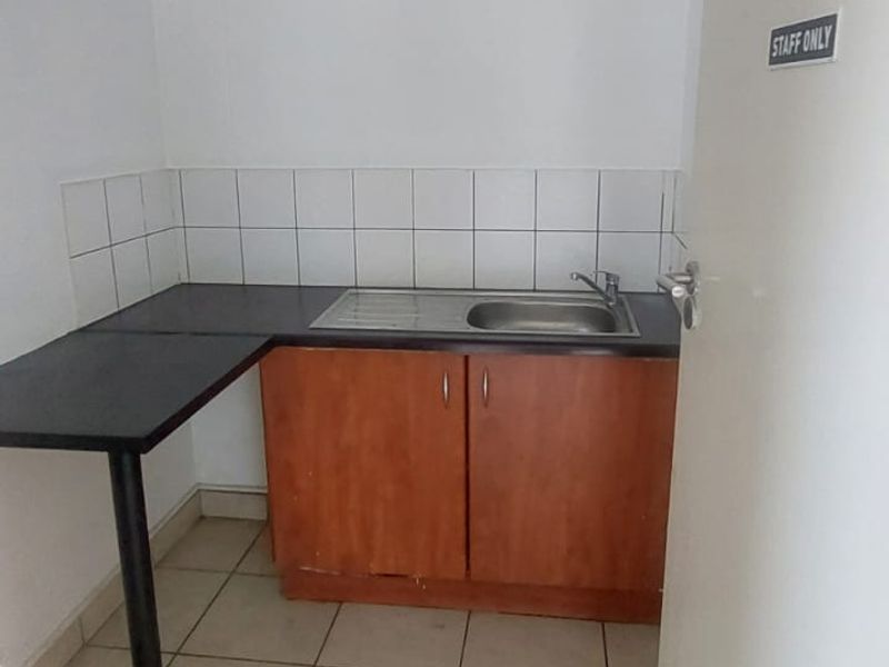 A compact staff kitchenette featuring a single sink, laminate countertop, and basic under-counter cabinetry with tiled splashbacks.