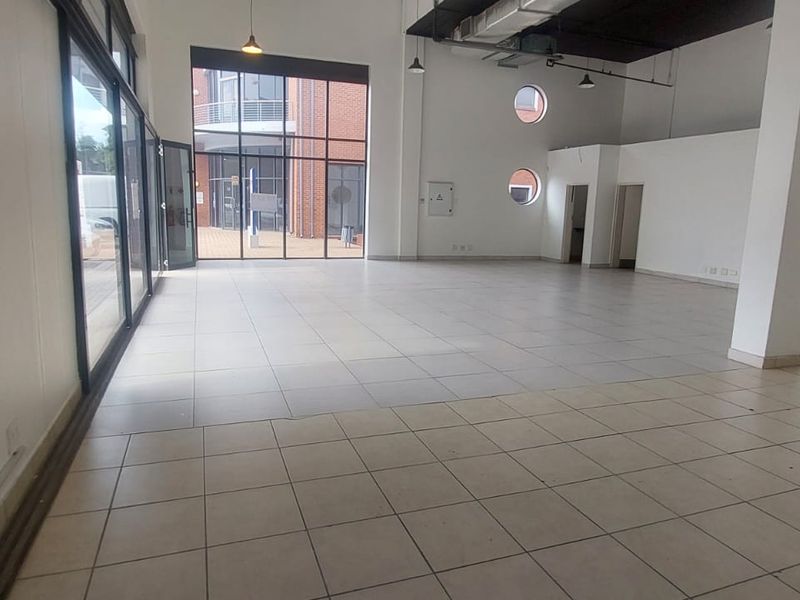 Spacious open-plan retail unit featuring high ceilings, large glass frontage, tiled flooring, and exposed industrial-style ducting.