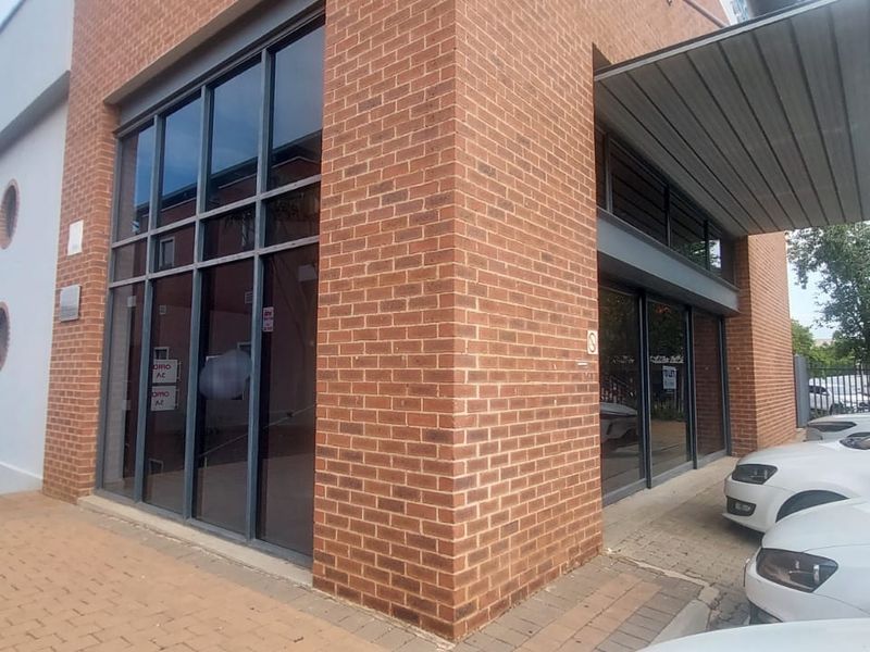 Exterior view of a modern retail building featuring red brick facade, large glass storefront windows, and a paved entrance area.