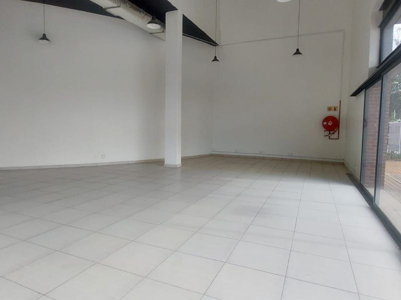 A spacious, open-plan retail unit featuring tiled flooring, high ceilings with exposed ducting, and large glass frontage providing excellent natural light and visibility.