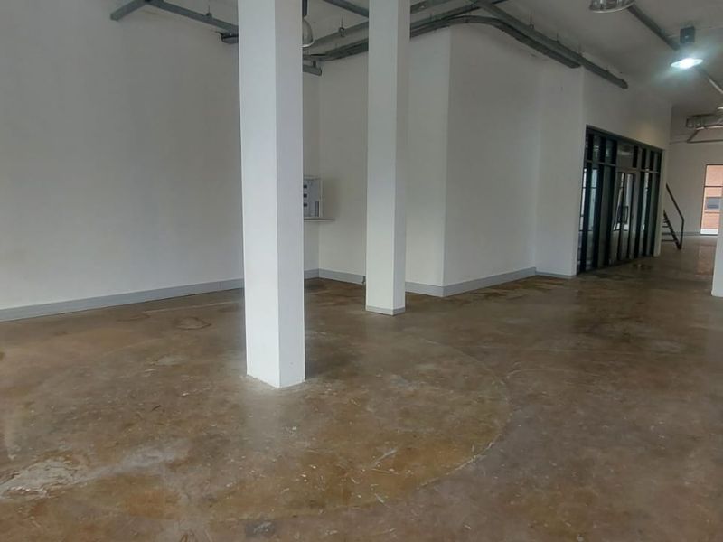 An open-plan retail space featuring exposed industrial ceiling ductwork, structural support columns, and polished concrete flooring, offering a versatile blank canvas for business.