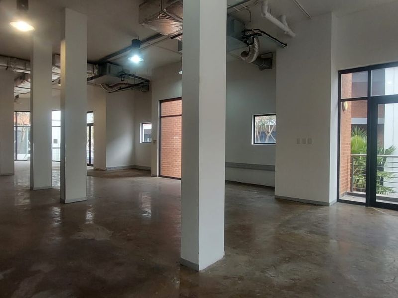 Spacious open-plan retail unit featuring high ceilings with exposed ducting, concrete flooring, and large glass doors providing ample natural light.