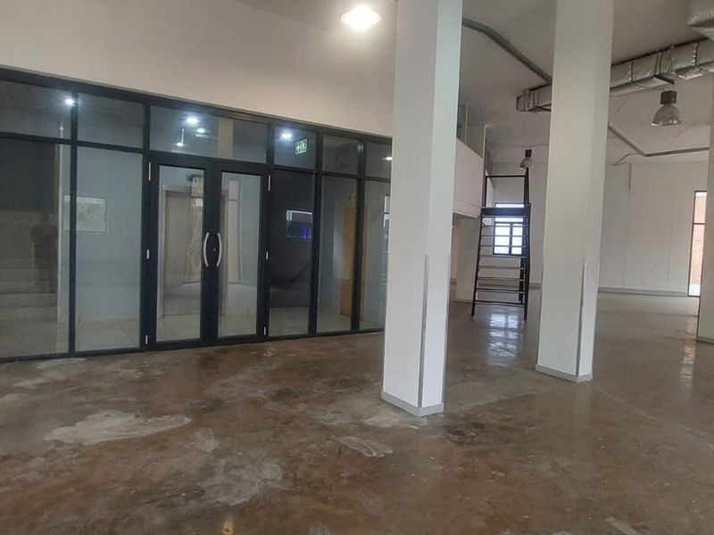 Spacious open-plan retail or commercial area featuring high ceilings, exposed ducting, large glass partitions, and polished concrete flooring.