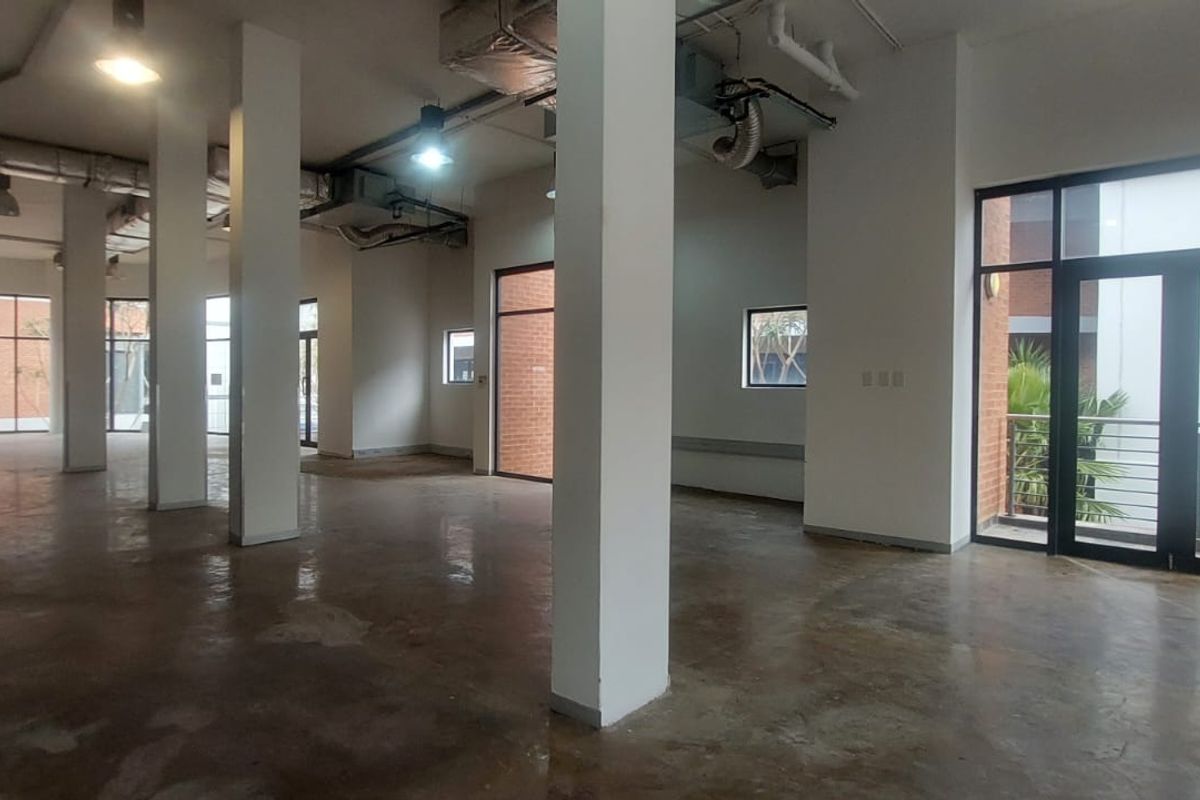 Spacious open-plan retail unit featuring high ceilings with exposed ducting, concrete flooring, and large glass doors providing ample natural light.