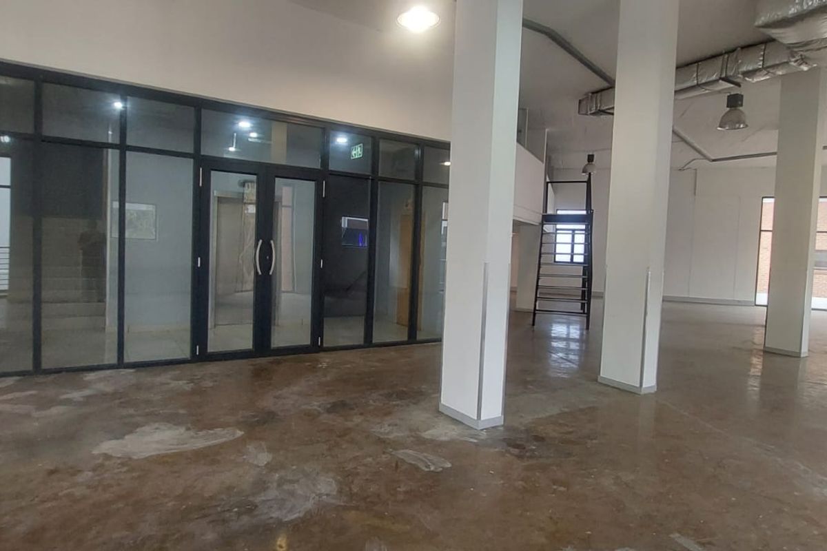 Spacious open-plan retail or commercial area featuring high ceilings, exposed ducting, large glass partitions, and polished concrete flooring.