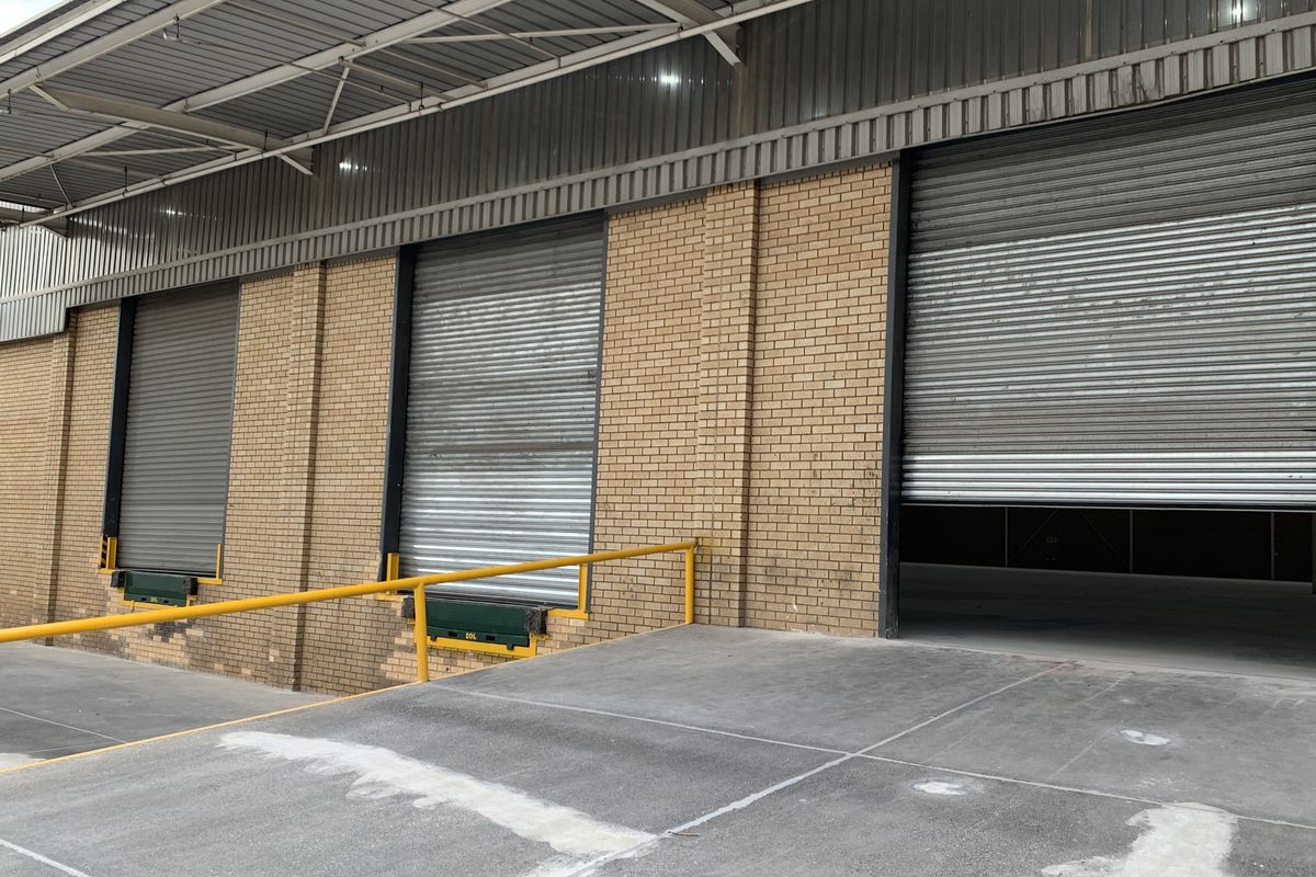 Industrial loading bay area featuring multiple roller shutter doors, a concrete loading ramp, and protective safety railings.