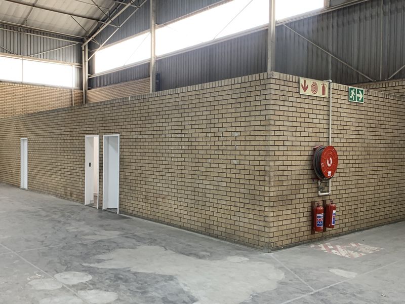 Spacious industrial utility area featuring exposed steel roof trusses, durable concrete flooring, and integrated fire safety equipment including a hose reel and extinguishers.
