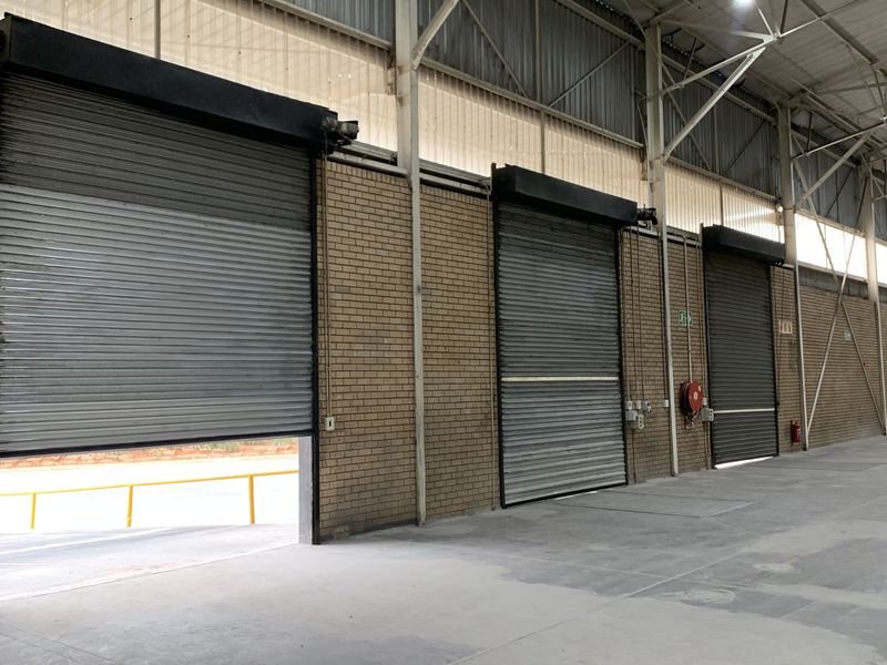 Spacious industrial warehouse interior featuring multiple roller shutter doors, exposed steel roof trusses, and durable concrete flooring, suitable for logistics or manufacturing operations.