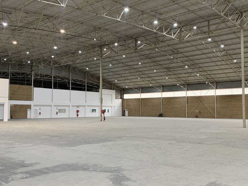 A large, open-plan industrial warehouse space featuring high-clearance steel roof trusses, durable concrete flooring, and integrated fire safety equipment.