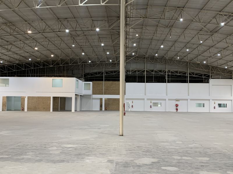Expansive industrial warehouse space featuring high ceilings with exposed steel trusses, high bay lighting, and integrated office partitioning.