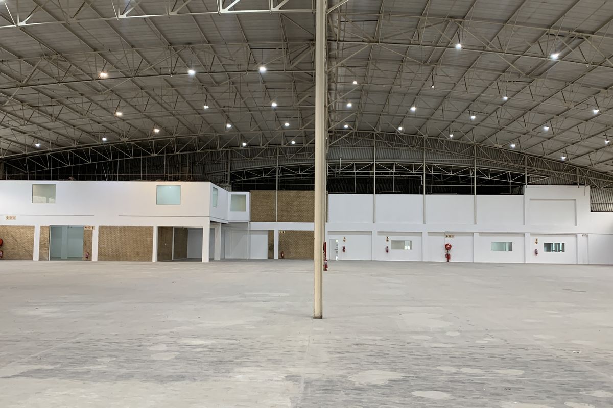 Expansive industrial warehouse space featuring high ceilings with exposed steel trusses, high bay lighting, and integrated office partitioning.