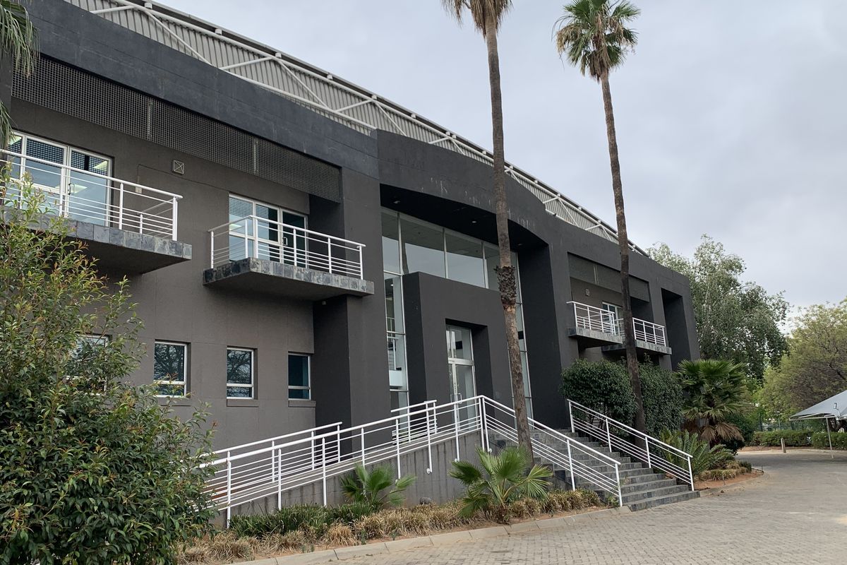 Modern industrial office building facade featuring a prominent entrance, wheelchair ramp, concrete staircase, and multiple balconies with metal railings.