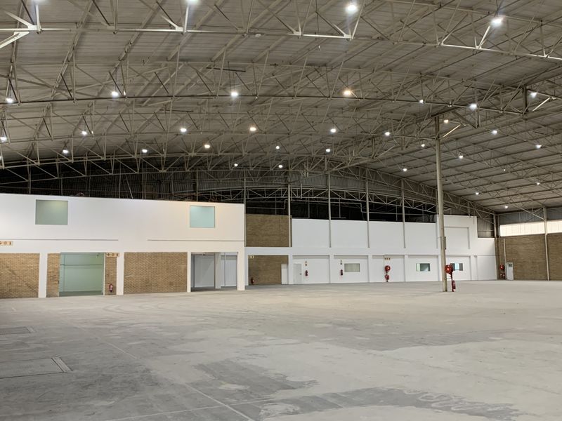 Spacious industrial warehouse featuring high-clearance steel roof trusses, polished concrete flooring, integrated office partitioning, and functional high-bay lighting throughout the open floor plan.